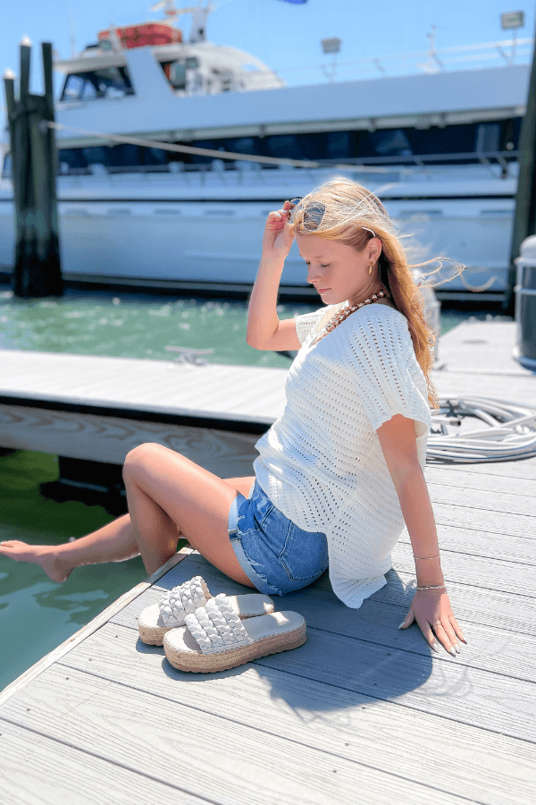 White Open Knit Crochet Sweater styled with denim shorts, perfect for summer lounging by the harbor. Lightweight and breezy for vacay vibes.