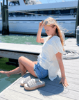 White Open Knit Crochet Sweater styled with denim shorts, perfect for summer lounging by the harbor. Lightweight and breezy for vacay vibes.