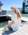 White Open Knit Crochet Sweater styled with denim shorts, perfect for summer lounging by the harbor. Lightweight and breezy for vacay vibes.