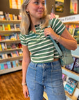 Easy A Green Striped Baby Tee with cropped fit and V-neck button detail, styled with high-waisted jeans in a bookstore setting.