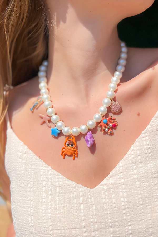Colorful Sea Life Charm Pearl Necklace worn with a white textured dress, showcasing whimsical ocean-themed charms on pearl beads.