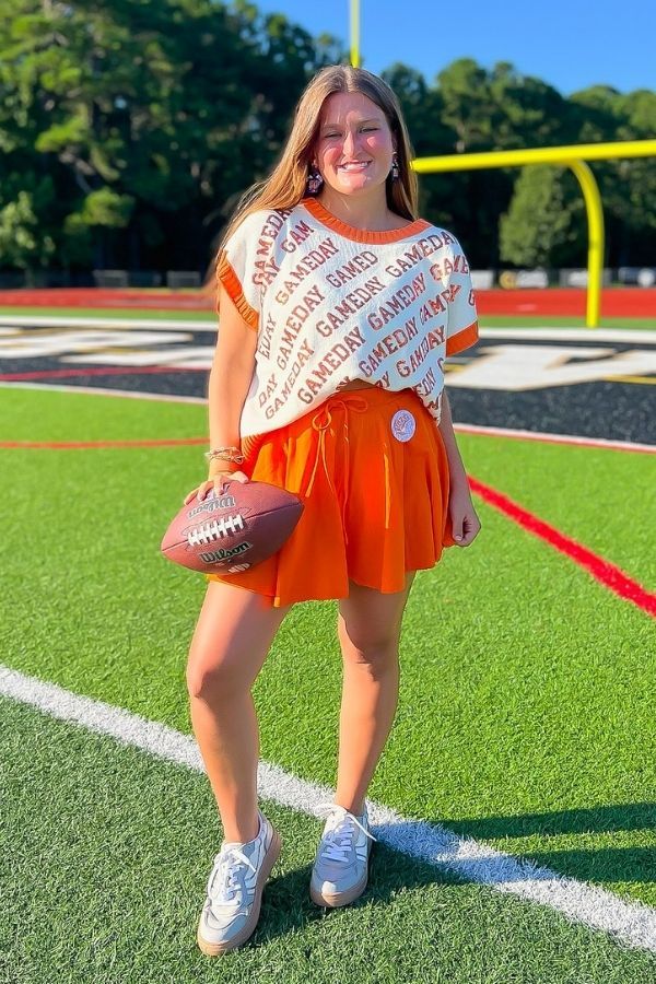 GAMEDAY Sequin Sweater Vest - Orange & White styled with orange skirt on football field. Collegiate knit vest perfect for spirited gameday looks.