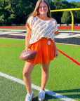 GAMEDAY Sequin Sweater Vest - Orange & White styled with orange skirt on football field. Collegiate knit vest perfect for spirited gameday looks.