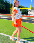 Model walking on football field in GAMEDAY Sequin Sweater Vest - Orange & White. Sleeveless knit vest styled for gameday fashion.
