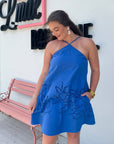 MINKPINK Royal Blue Darla Broderie Mini Dress with halter neckline and floral embroidery, styled for summer chic in front of boutique.