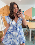Meet Me in Santorini Coastal Sketch Dress in blue and white Mediterranean print, shown in a casual indoor setting with mirror selfie.