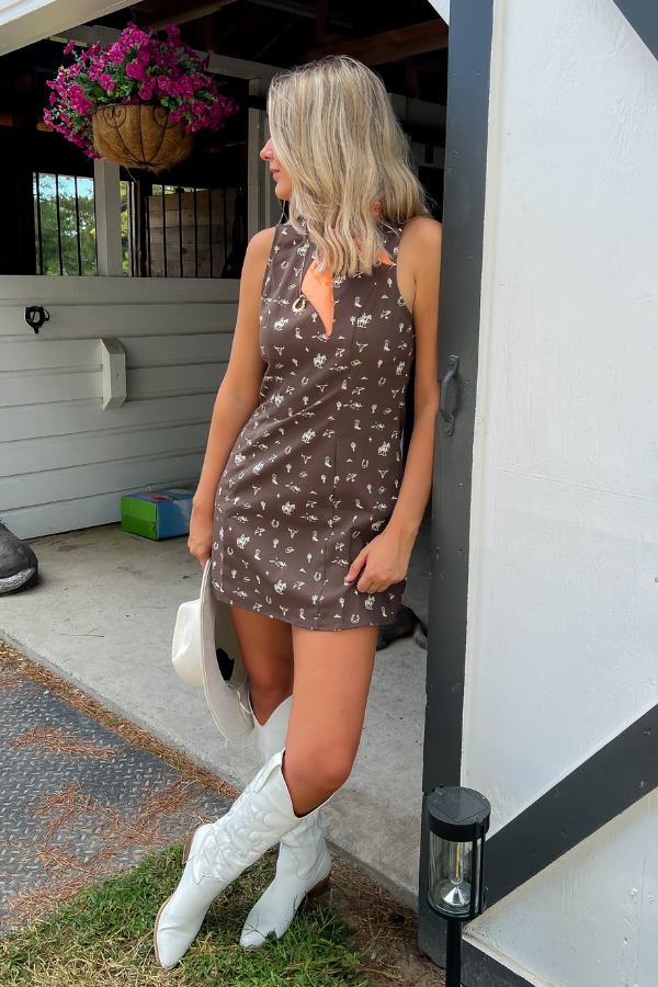 Giddy Up Brown Cowboy Print Mini Dress styled with white cowboy boots and orange bandana, perfect for a country concert outfit.