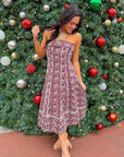 Scarlet Garden Floral Strapless Dress in burgundy with white embroidery, styled for a holiday occasion in front of a Christmas tree.
