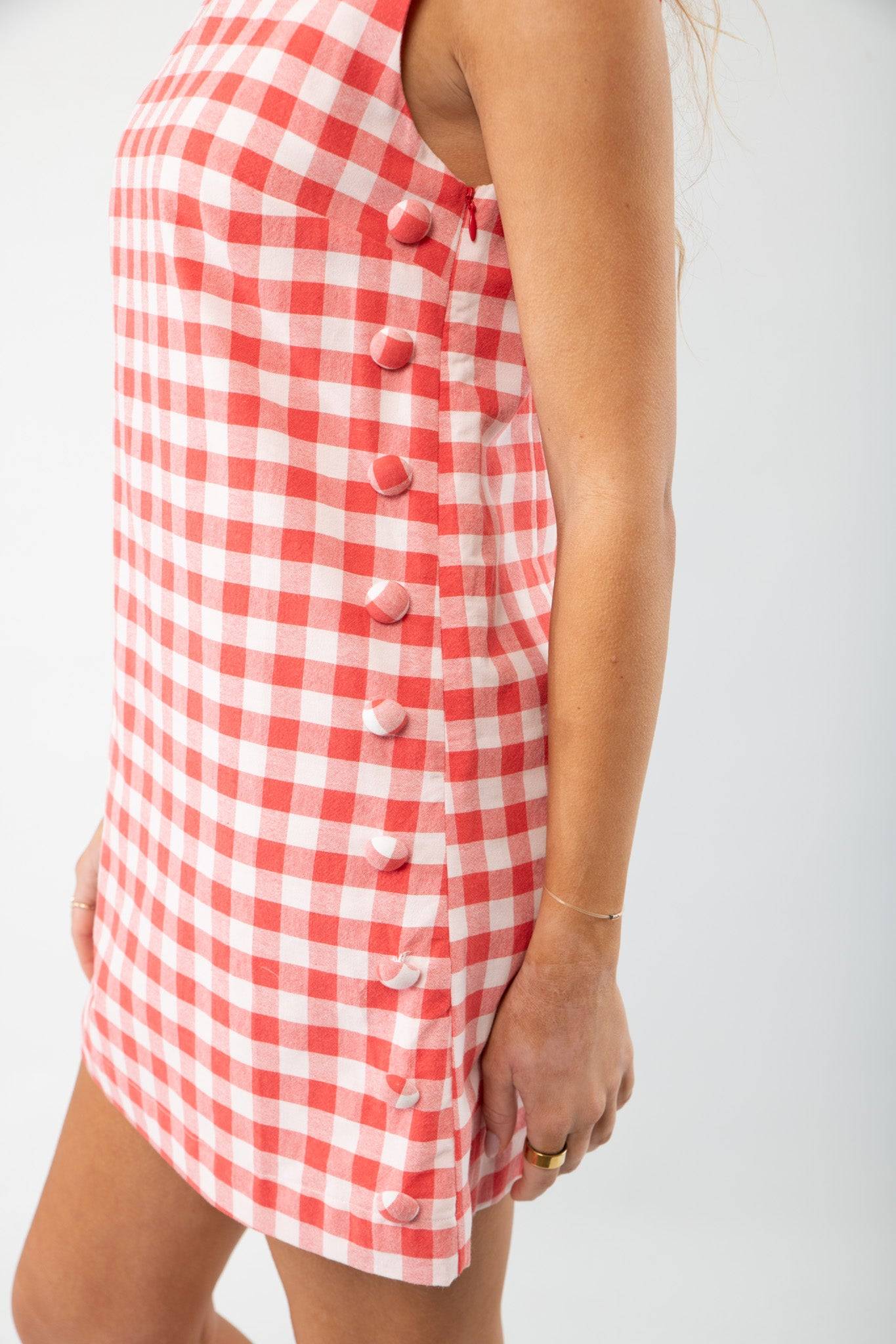 Close-up of Poppy Red Gingham Mini Dress side button detail, showcasing its playful pattern and tailored fit for casual summer wear.