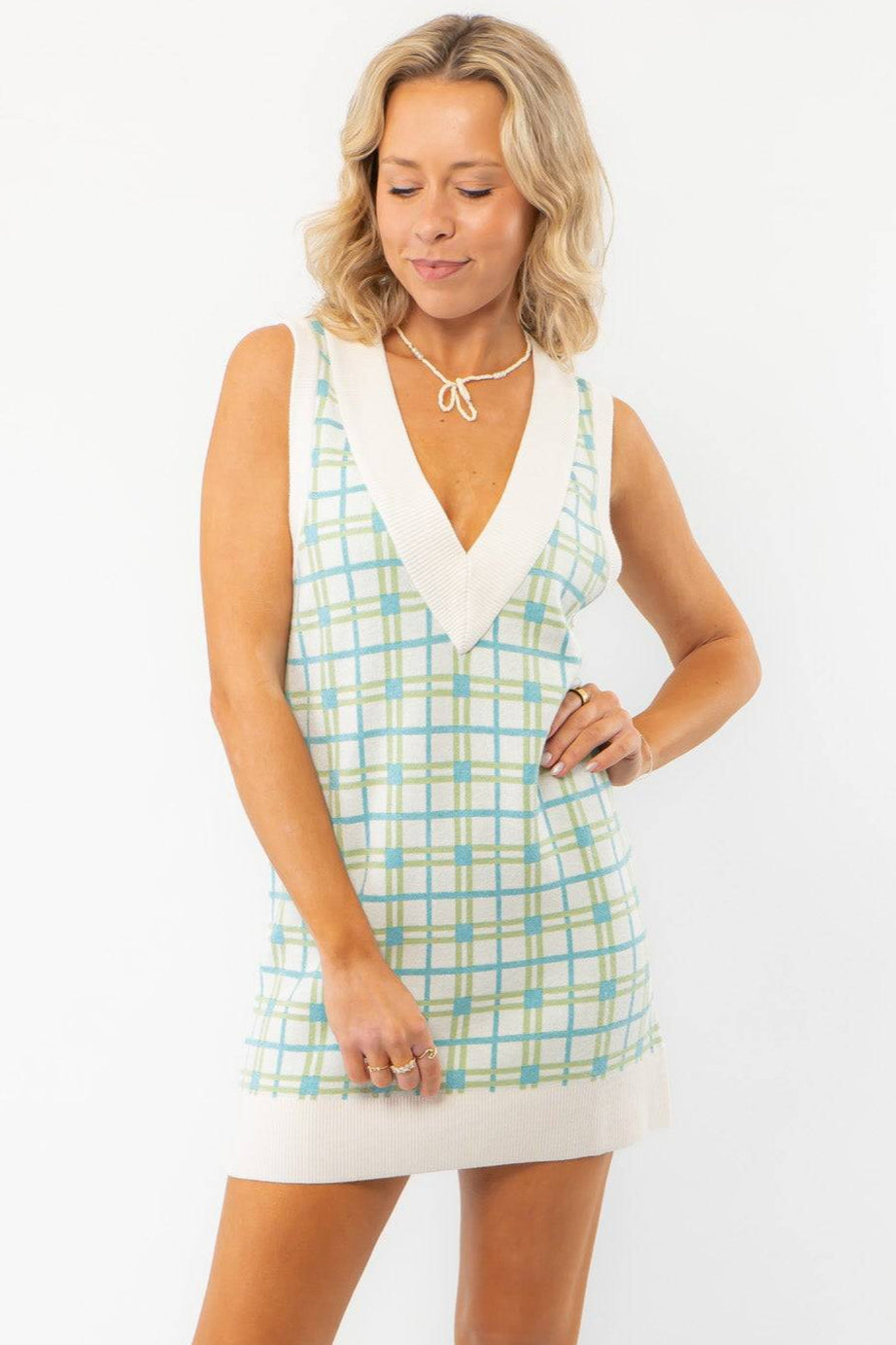 Show Me Your Mumu Green Plaid Knit Hartford Tank Sweater Dress with a V-neckline and relaxed fit, styled with beige loafers and socks.