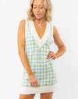 Show Me Your Mumu Green Plaid Knit Hartford Tank Sweater Dress with a V-neckline and relaxed fit, styled with beige loafers and socks.