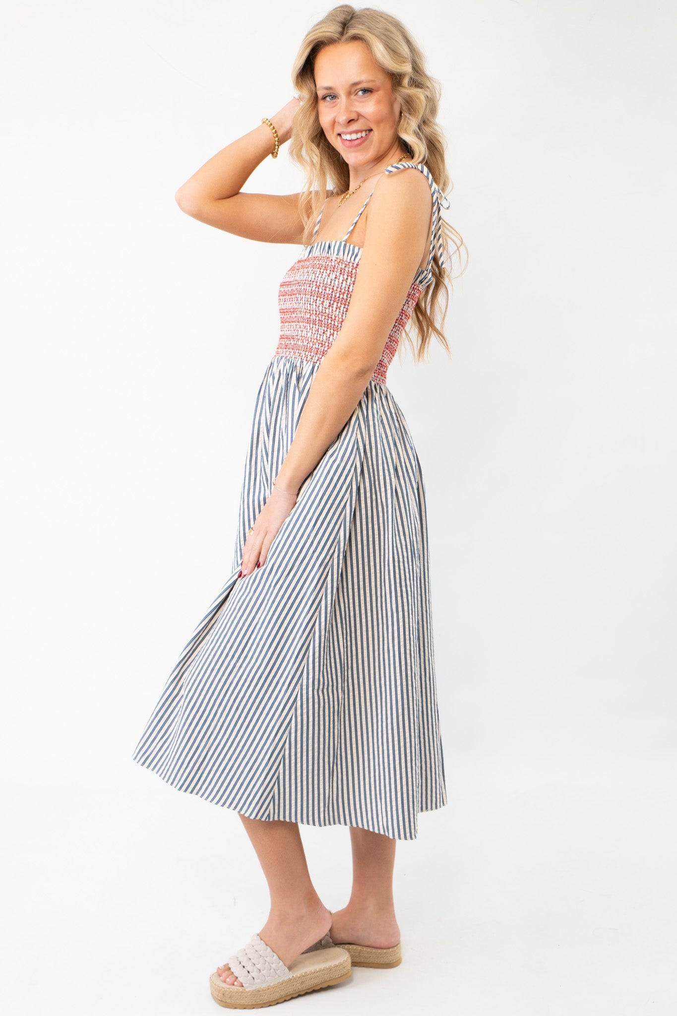 Model posing in THML Smocked Blue Striped Tie Strap Midi Dress, highlighting its flattering fit and breezy silhouette for warm-weather occasions.
