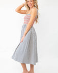 Model posing in THML Smocked Blue Striped Tie Strap Midi Dress, highlighting its flattering fit and breezy silhouette for warm-weather occasions.