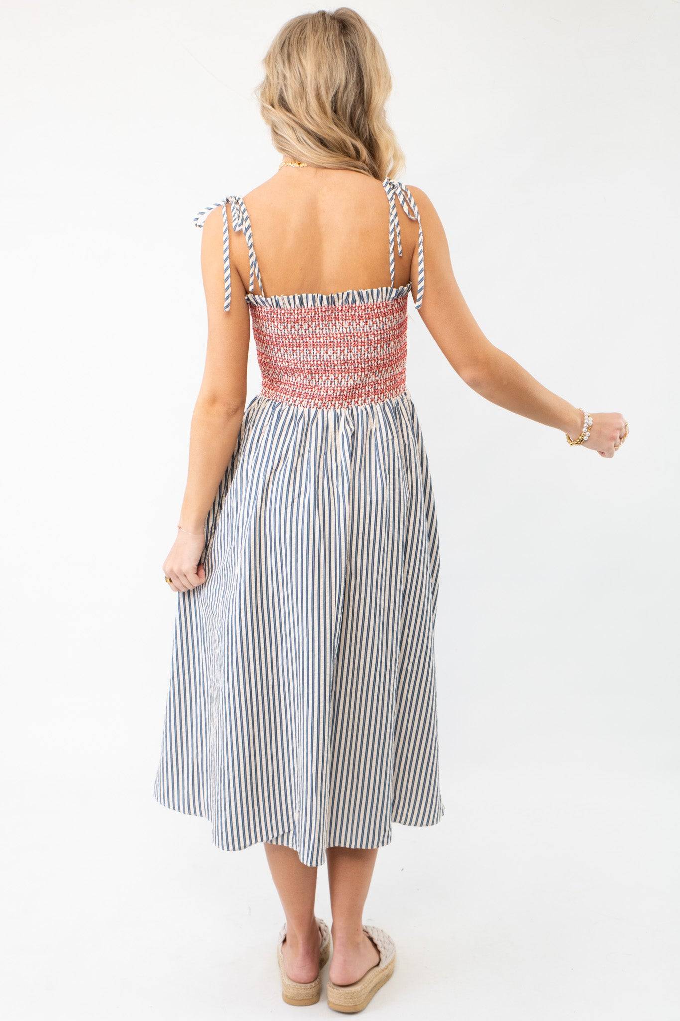 Back view of THML Smocked Blue Striped Tie Strap Midi Dress with red smocked top and striped skirt, a chic and comfortable summer dress option.