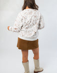Back view of Snuggle Pup Dog Print Sweatshirt featuring all-over brown puppy illustrations on a white crewneck, paired with a suede mini skirt.