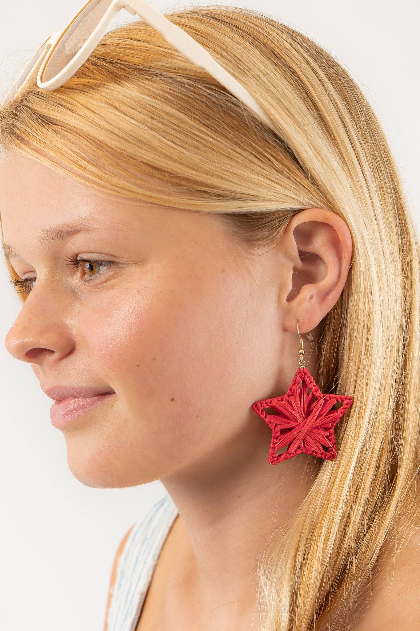 Model wearing Red Raffia Star Earrings with a casual summer outfit, showcasing lightweight, statement jewelry perfect for beach days and BBQs.