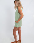 Back view of the green gingham mini dress with sleeveless cut, showing fit and style, paired with sunglasses and platform sandals
