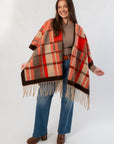 Fireside Plaid Shawl draped over shoulders, showcasing its vibrant orange plaid pattern and fringe hem for a cozy fall look.
