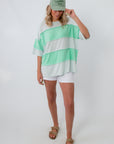 Model wearing Seaglass Shine mint green oversized striped knit top with white shorts and beige sandals