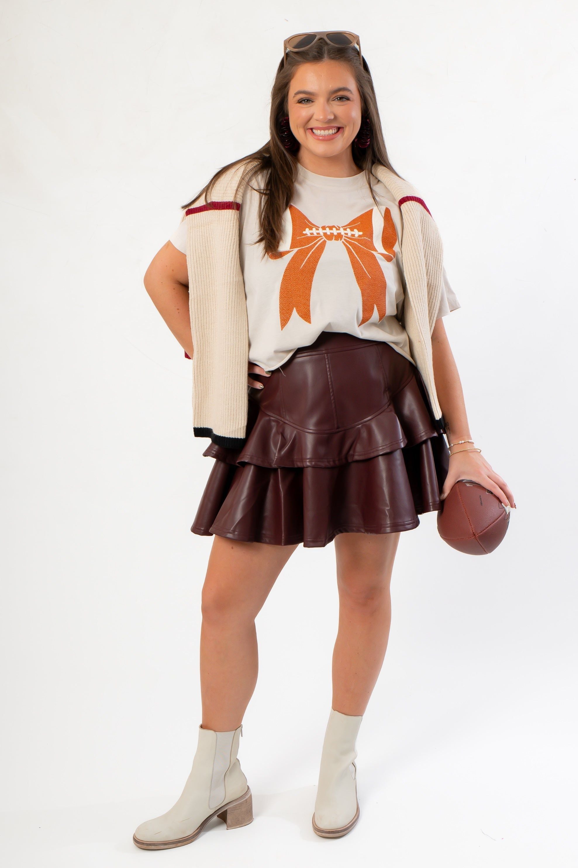 Game Fashion look featuring the Goal Line Football Tee with bone bow print, layered with a sweater and styled with boots and a leather skirt.