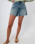 Close-up of high-rise denim shorts with frayed hem, worn with green sweatshirt