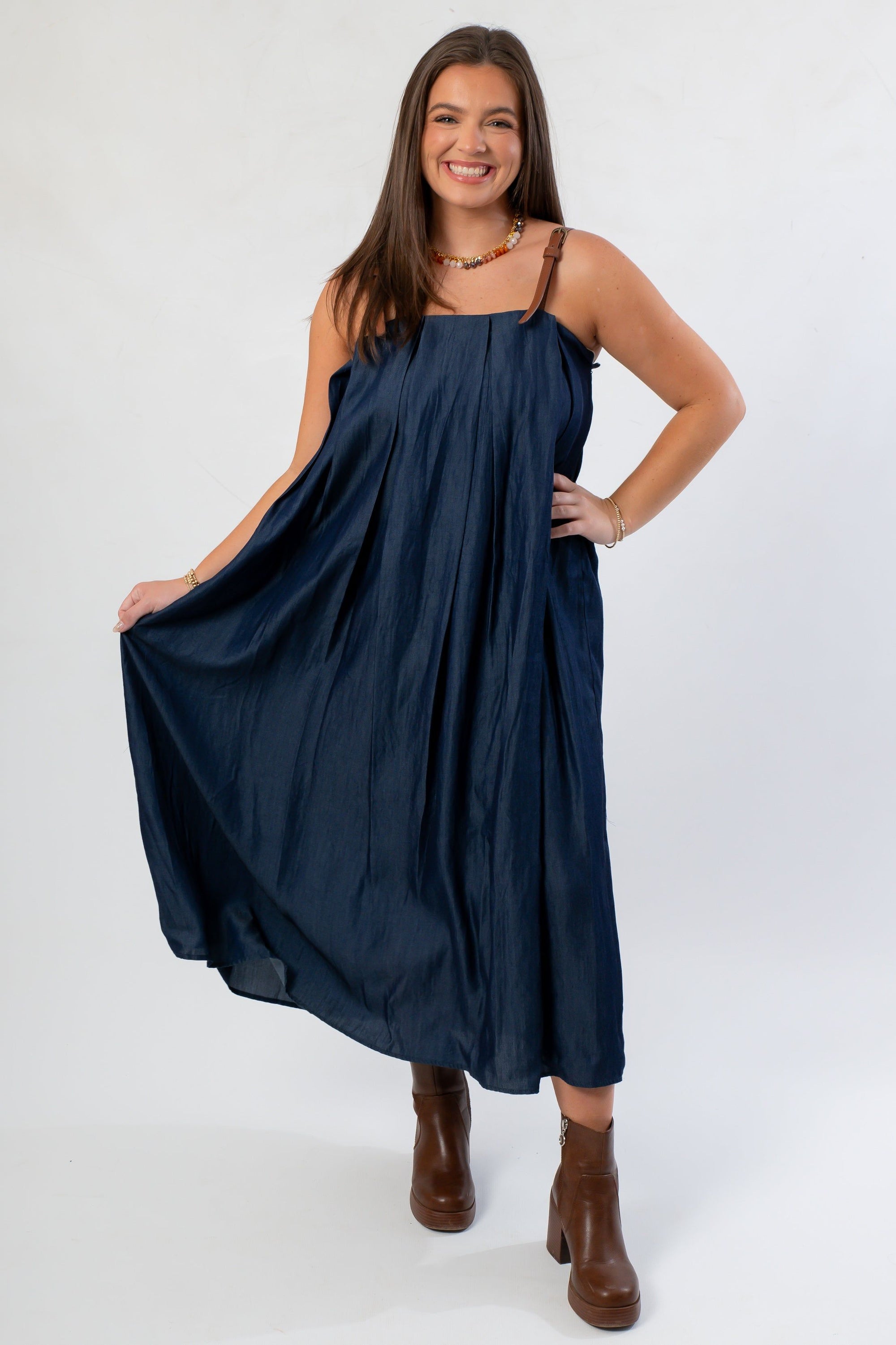 Denim Buckle Strap Dress by THML in midi length, featuring pleated design and adjustable brown straps, paired with heeled boots.