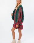 Side view of Frosted Pine Green Faux Fur Vest layered over a red plaid dress, showcasing cozy winter outerwear for women.