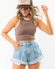 Model wearing In Your Dreams Brown Cropped Tank Top with contrast seams and casual denim shorts, accessorized with a western-style cap.