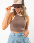 Close-up of In Your Dreams Brown Cropped Tank Top featuring white embroidered text and cream trim, paired with high-waisted denim shorts.