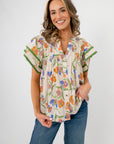 Spring Fling Floral Ruffle Sleeve Blouse in ecru with colorful floral print and green-trimmed ruffle sleeves, styled with blue jeans.
