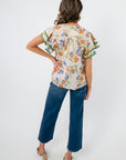 Back view of Spring Fling Floral Ruffle Sleeve Blouse in ecru with colorful floral print and green-trimmed ruffle sleeves, styled with denim jeans.