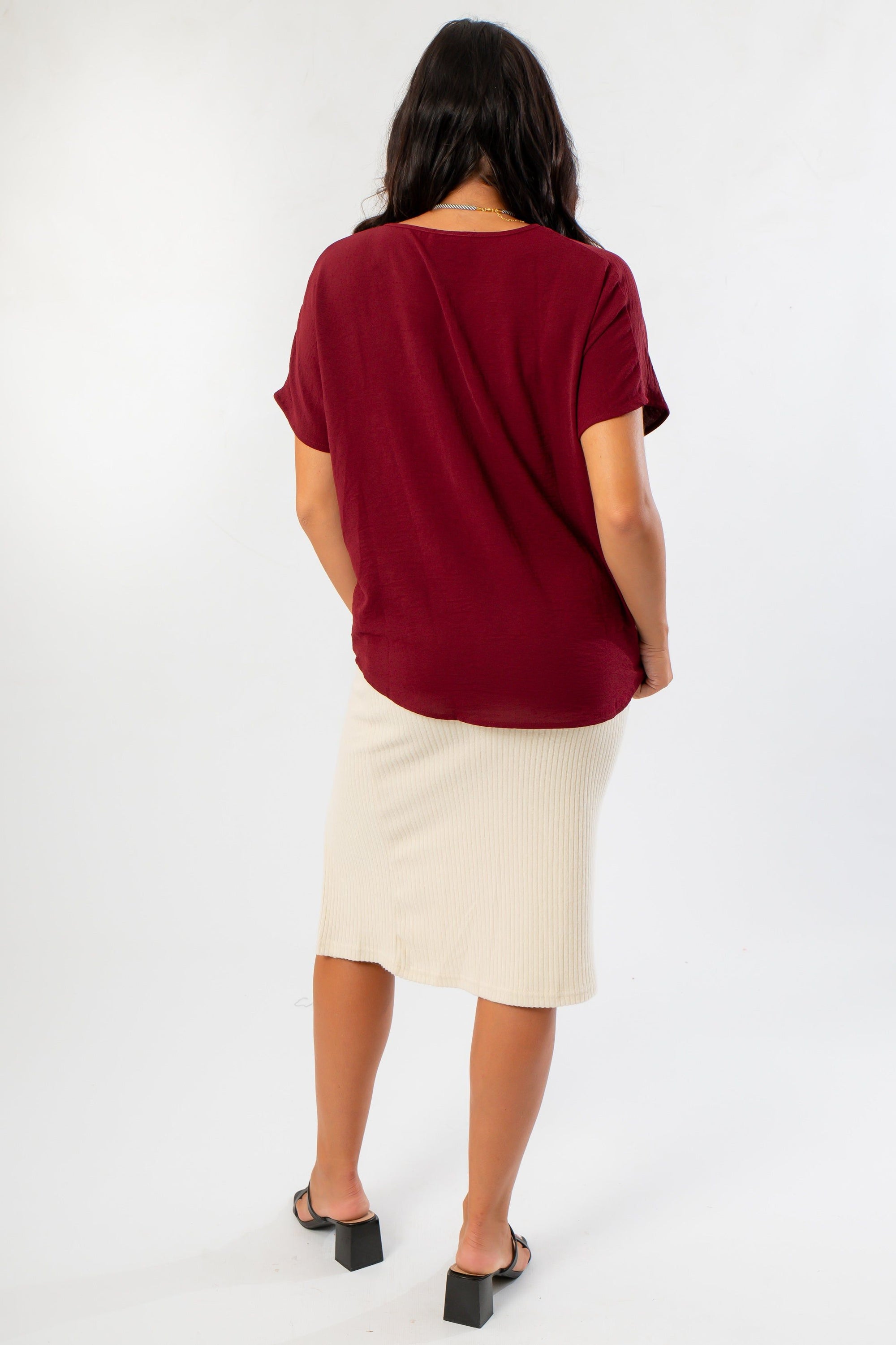 Back view of Burgundy Short Sleeve Blouse highlighting its loose fit and soft fabric, styled with a cream midi skirt for a cozy fall look.