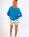 Back view of Hit The Slopes Blue & Orange Ski Sweater highlighting its cozy knit texture, paired with polka dot shorts and winter accessories.