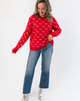 Boutique holiday style red Christmas sweater featuring festive 'ho' print, paired with flared jeans and silver ankle boots.
