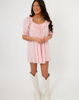 Show Me Your Mumu Pink Eyelet Toulouse Dress with ruffled neckline and puff sleeves, styled with white boots for a casual spring look.