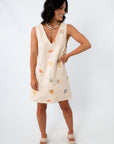 Full-body view of woman in Coastline Romance beach patterned shift dress with shell and starfish print, paired with beige crochet-strap heels.