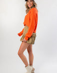 Side view of Orange Knit Crop Sweater with khaki ruffle skirt and neutral boots, highlighting trendy fall layering style.