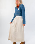 Side view of Denim Long Sleeve Top styled with a cream skirt and brown boots. A versatile, lightweight layering piece for casual outfits.