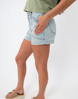 Back view of light wash denim shorts with classic pockets, high waist, and rolled cuffs, styled with a green top for summer casual look