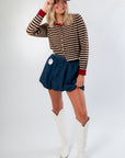 Jenna Brown & Burgundy Stripe Cardigan with thin knit stripes and red cuffs, styled with denim skirt and white boots for casual fall look.
