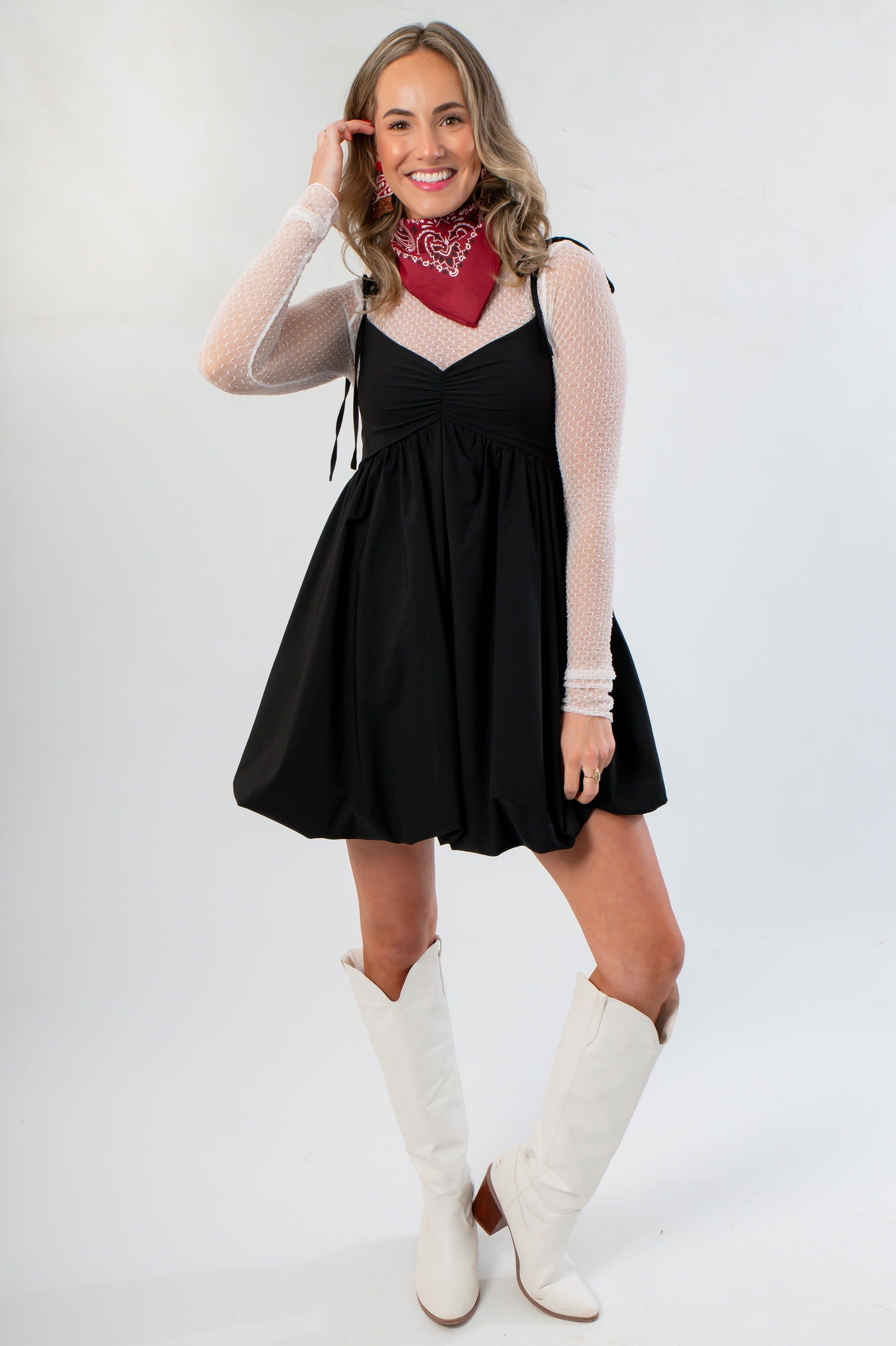 Elegant Black Bubble Hem Mini Dress with ruched bust and tie straps, paired with white boots and red bandana for a stylish casual outfit.