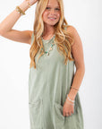 Sage green tank romper with a relaxed fit and front pockets, accessorized with sunglasses and bracelets for a chic summer outfit.
