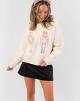Twin Tidings Nutcracker Sweater – Cozy cream holiday knit top with colorful nutcracker graphics, styled with a black mini skirt.