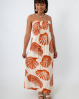 Side view of woman in orange shell print maxi dress with shell jewelry