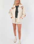 Model wearing Falling Back Cream Faux Leather Skort styled with embroidered jacket and boots, perfect for holiday or gameday looks.