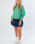 Emerald green cropped knit sweater featuring long sleeves and relaxed silhouette, paired with a navy mini skirt and cream boots.