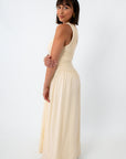 Back view of woman in cream maxi dress with keyhole back detail, standing with hand on hip