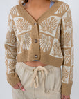 Cowrie Cutie Seashell Cardigan in taupe and ivory with seashell knit pattern, cropped fit, and button front, styled with neutral drawstring pants.