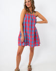 Woman wearing a red and blue plaid mini dress with spaghetti straps and pockets, standing against a white background