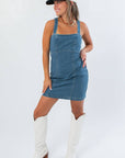 Karli Denim Corset Back Mini Dress in medium wash styled with white boots and a cap, perfect for a fitted gameday look.